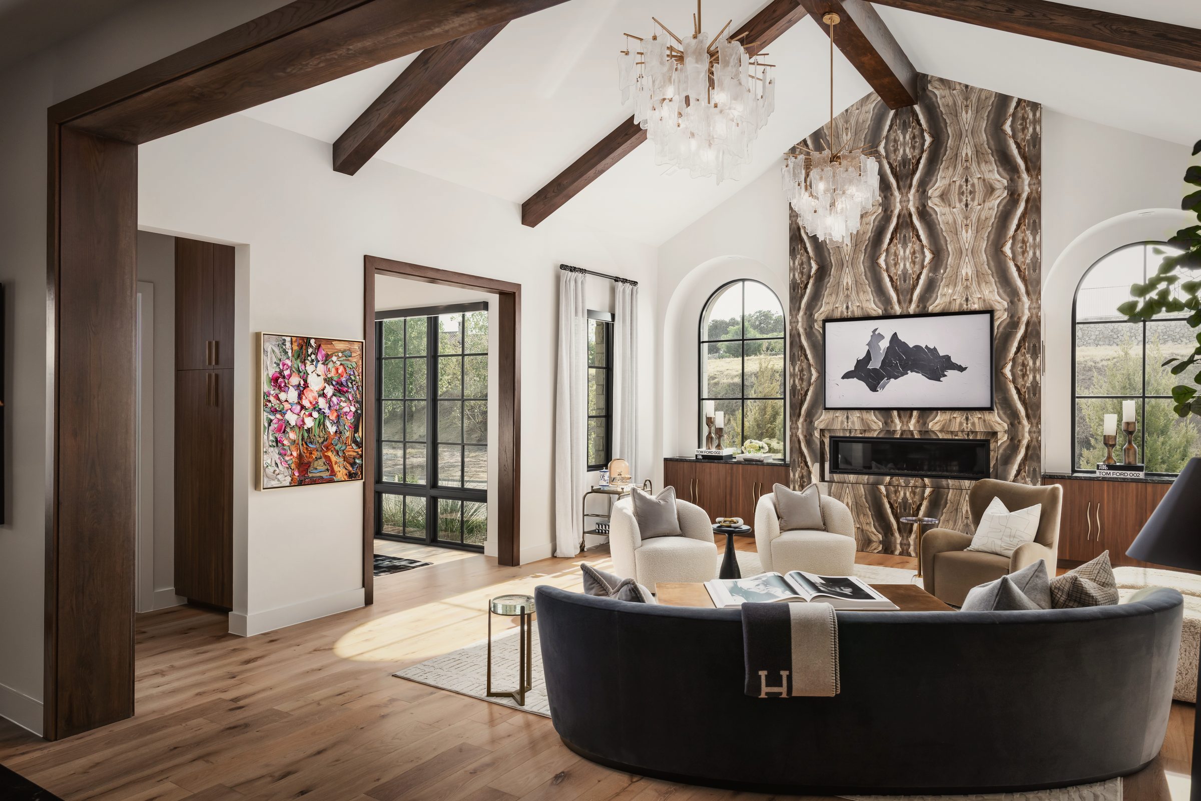 Vaulted living room with dark wood beams, a curved navy sofa, a crystal chandelier and a stone fireplace wall