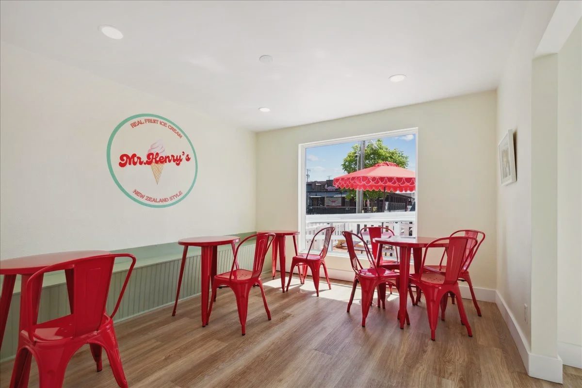 Ice cream shop seating room with red metal chairs and tables, the Mr. Henry's logo on the wall and a window onto red umbrellas