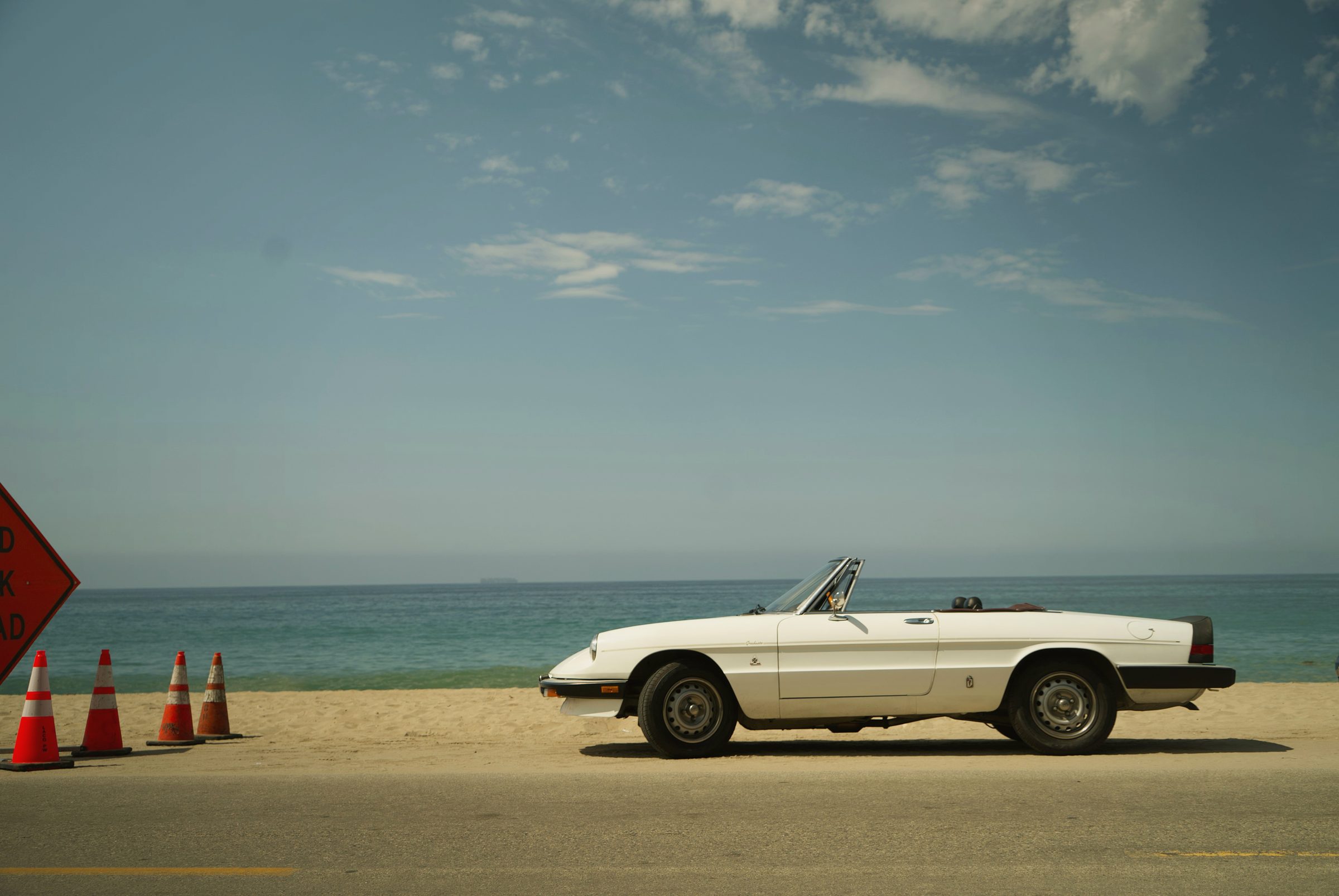A white vintage convertible parked on the sand by the ocean