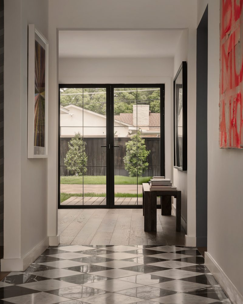 White hallway with red artwork on one wall, a black-and-white checkered floor and glass doors to the yard