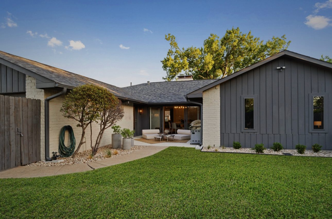 Back of the house across the lawn: white brick and dark board-and-batten, with a covered patio