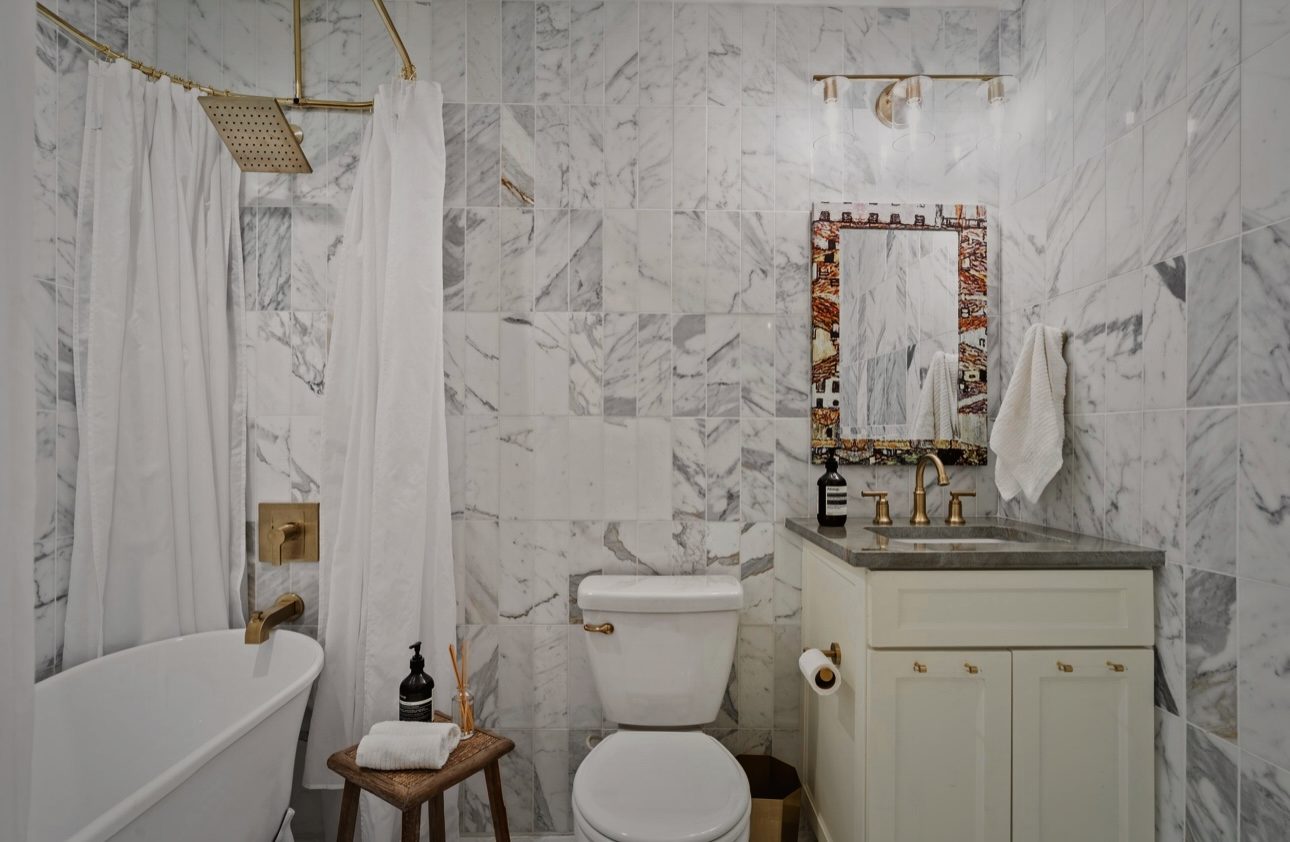 Bath with a white freestanding tub, marble tile and a brass mirror