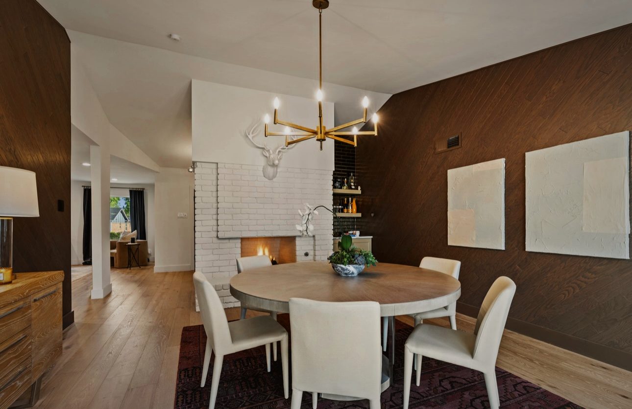 Dining room with a round table, a brass chandelier and a white brick fireplace with a white stag head