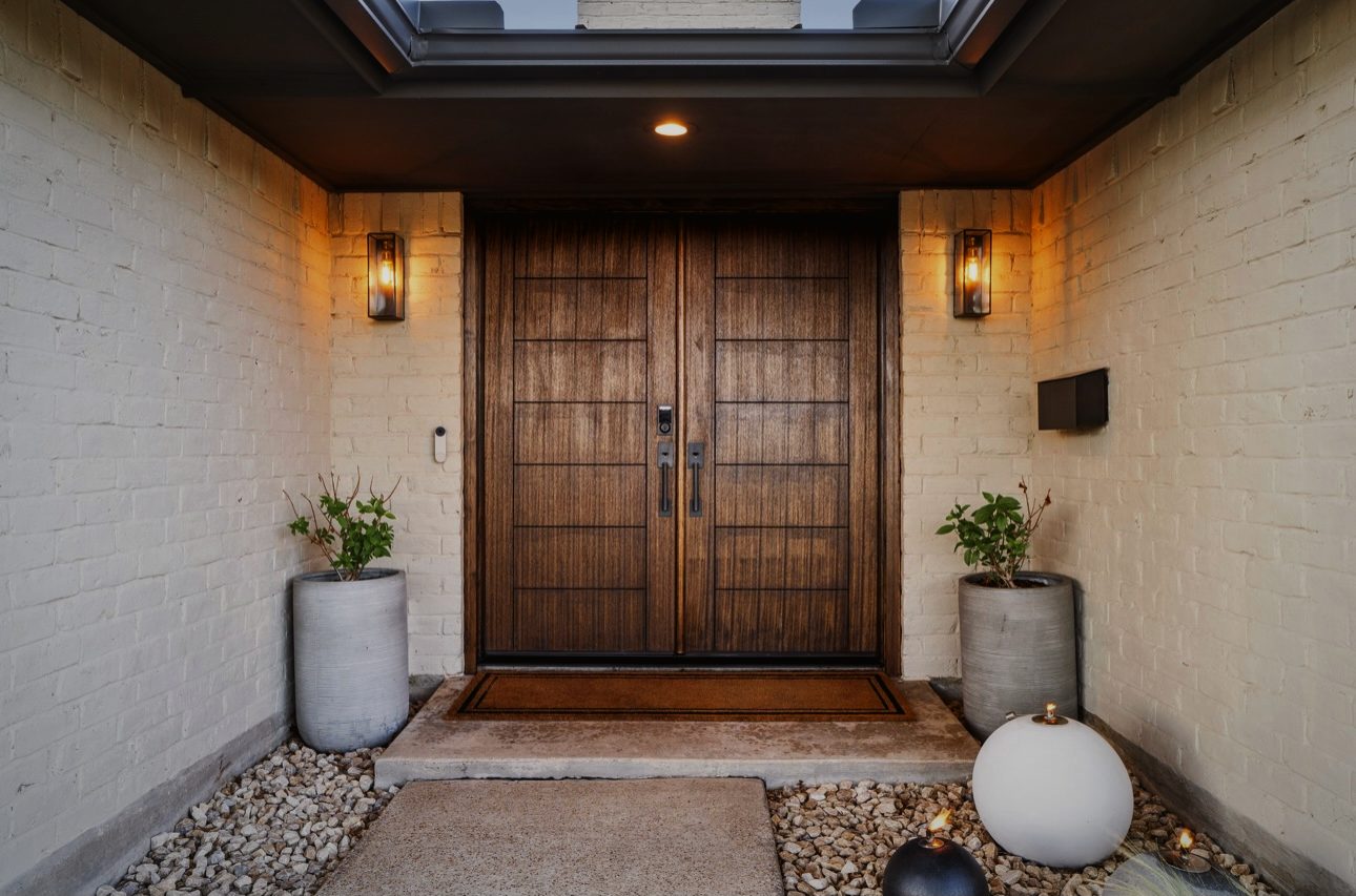 Covered entry with tall wood double doors, black lanterns, white brick and potted plants
