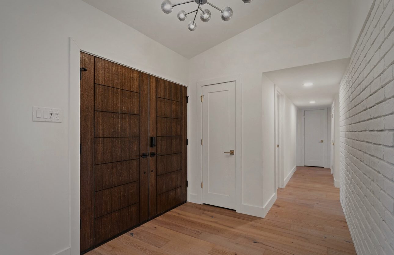 Foyer with the wood double doors, a white painted brick wall and a modern brass light