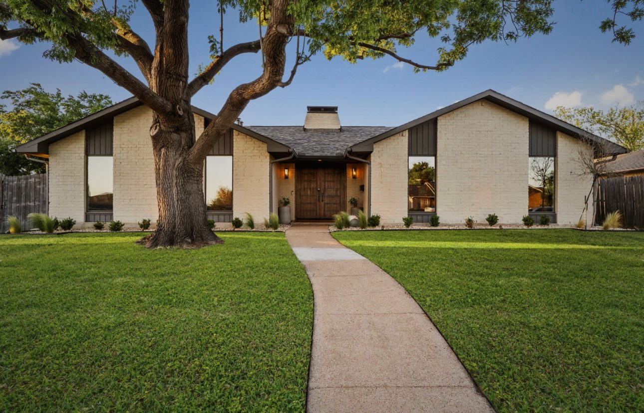 Front of the house: white brick with dark board-and-batten gables, a large oak and a walk across the lawn