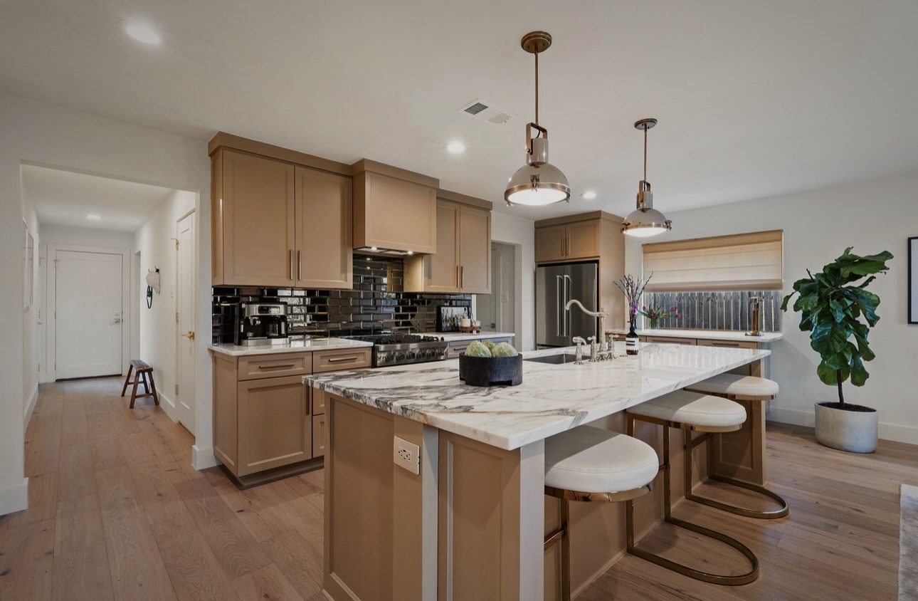 Kitchen with wood cabinets, a marble island with white stools, black tile and industrial pendants