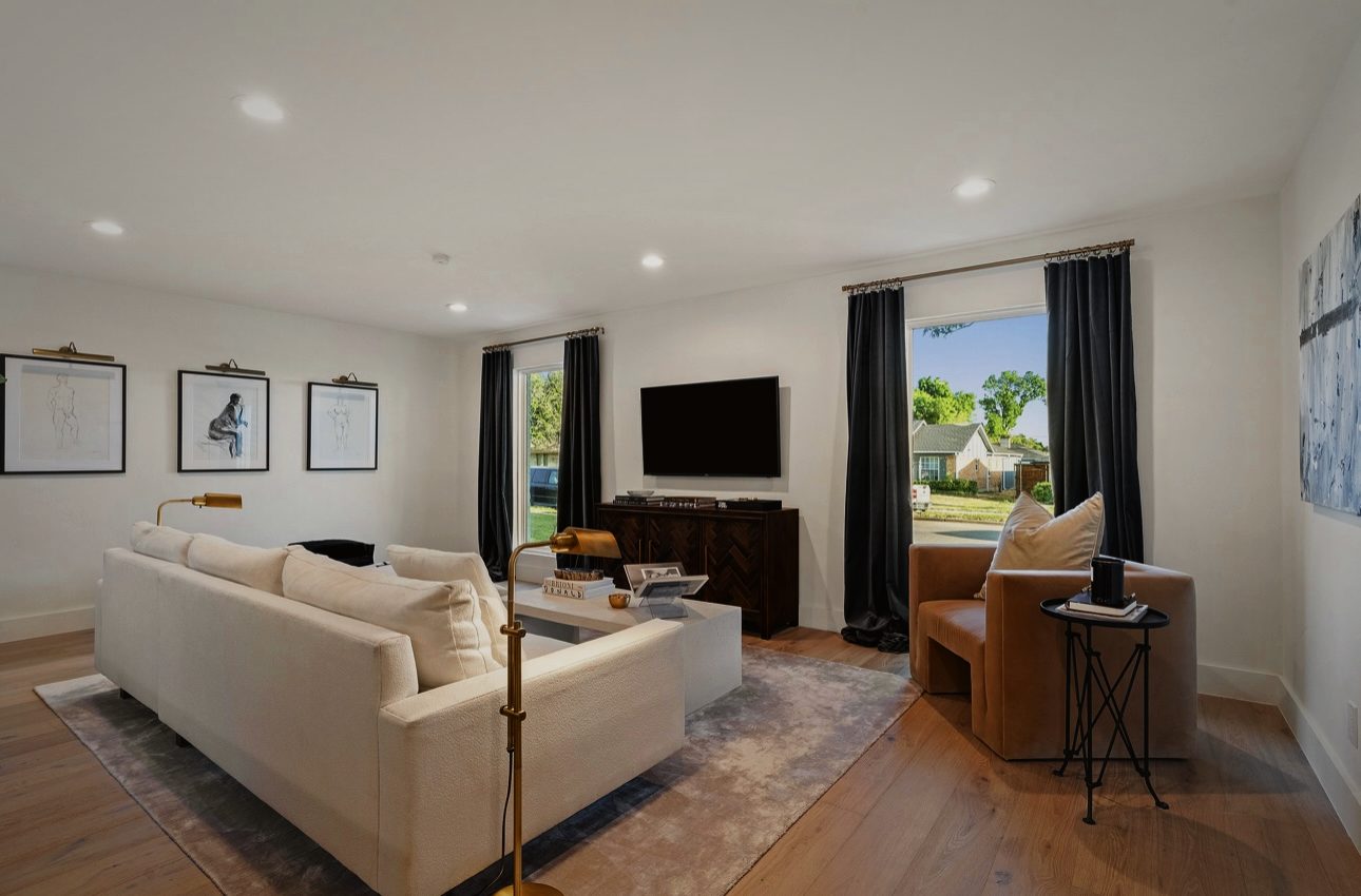 Living room with a white sofa, a leather chair, a dark wood console and a large window with black curtains