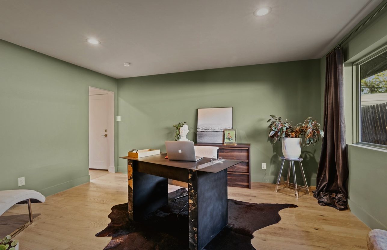 Office painted sage green with a dark wood desk, a cowhide rug and a plant by the window