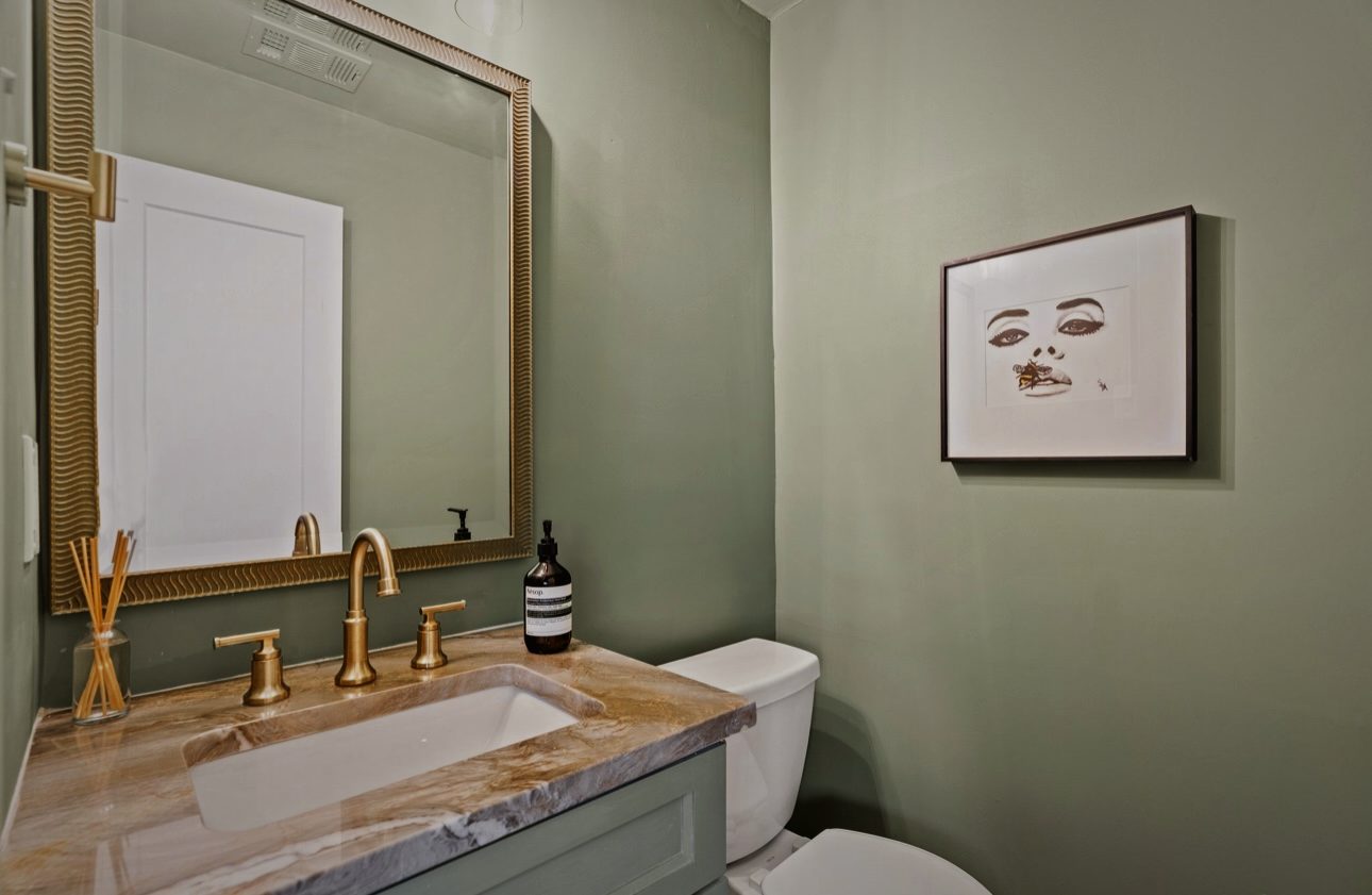 Sage powder room with a brass mirror, brass faucet and a framed drawing
