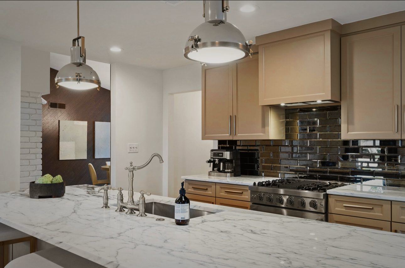 Range wall with black glass tile, wood cabinets and a marble counter under a large metal pendant