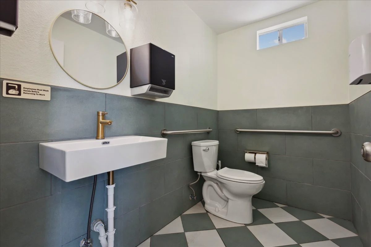 Restroom with sage green tile, a green and white checkered floor, a round mirror and a white trough sink