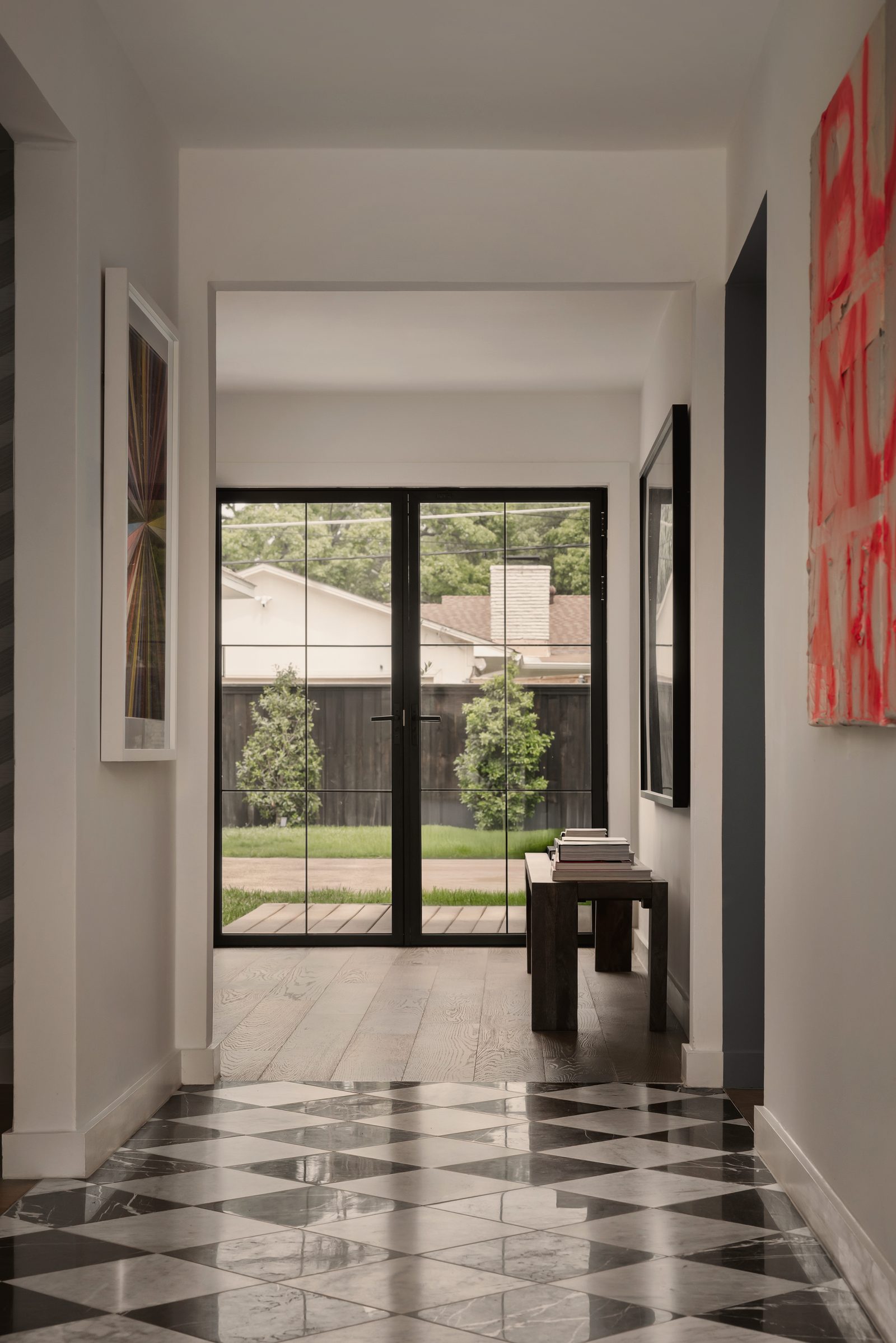 Hallway with a gray and white checkered marble floor, a large red text painting and black steel doors to the backyard