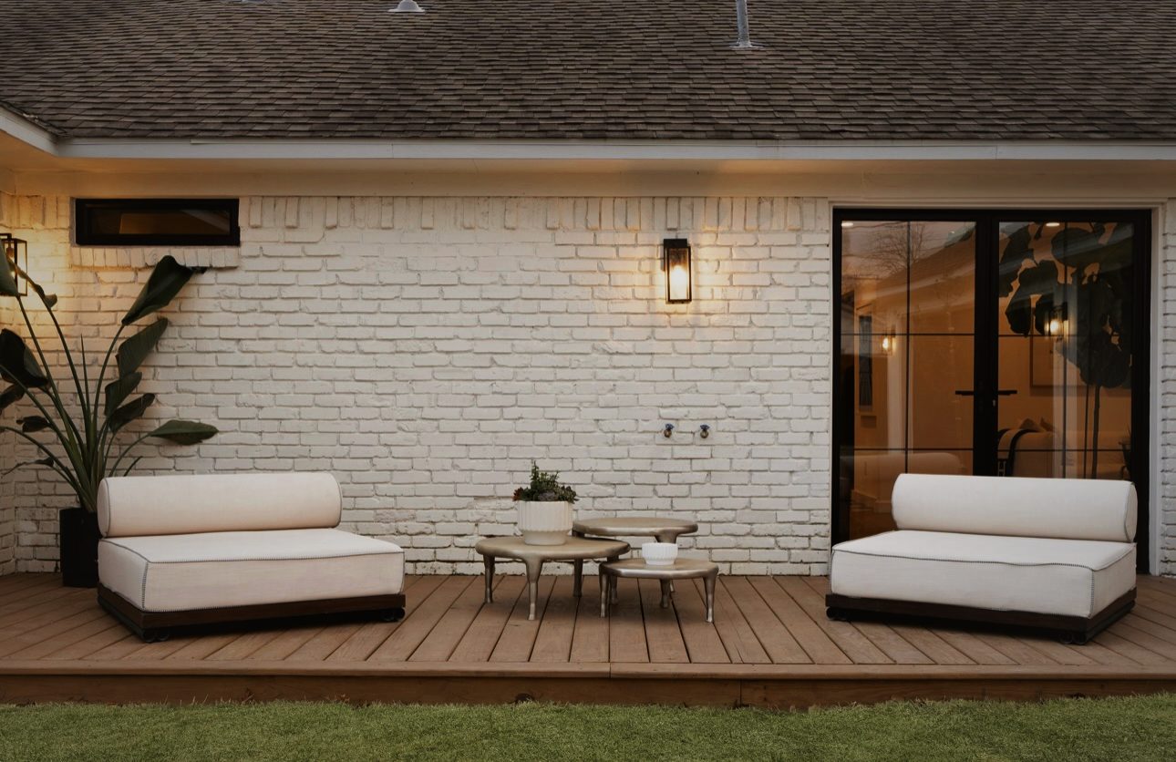 Wood deck against the white brick back of the house with two white lounge chairs and a low table
