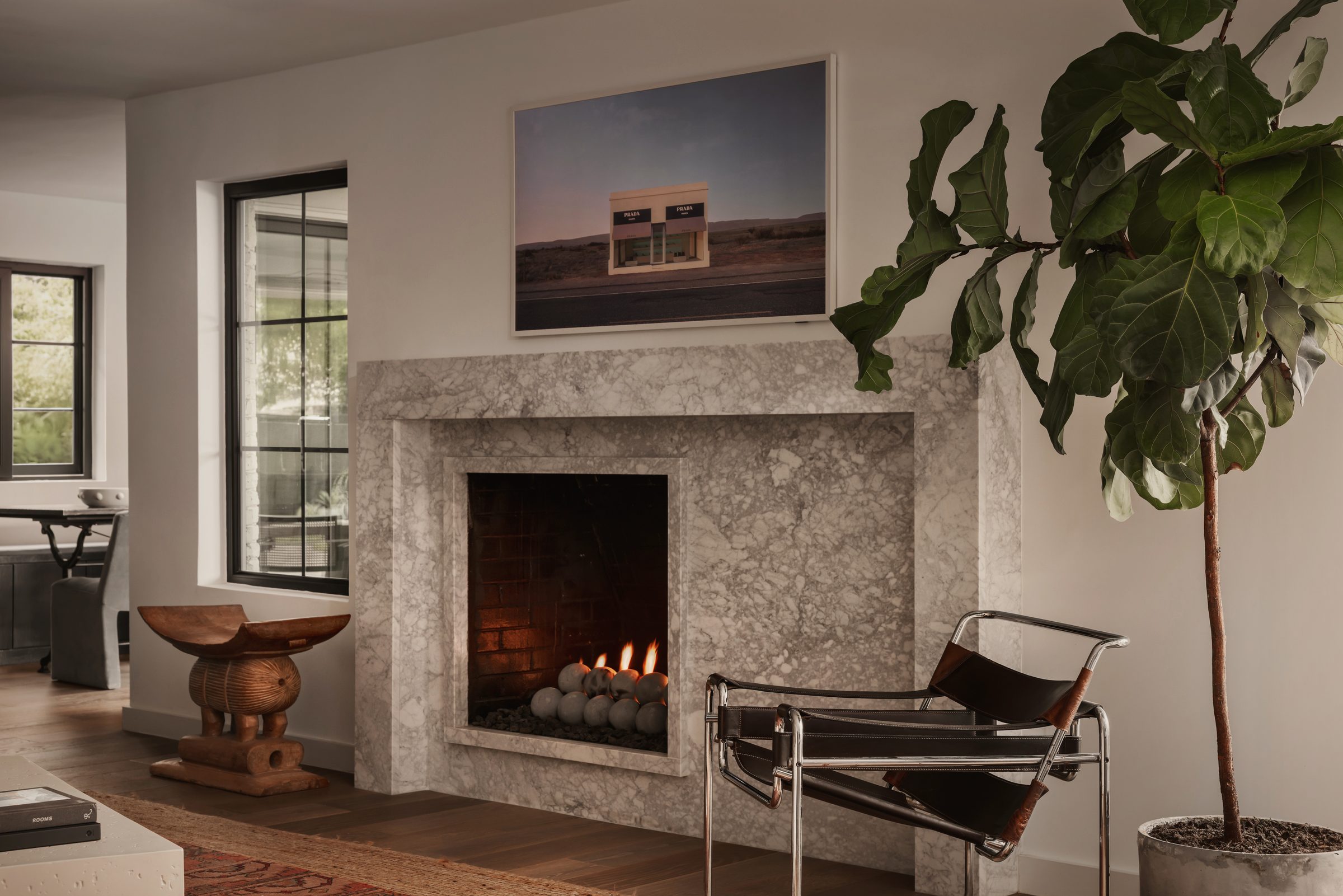 Marble fireplace with a desert photograph above it, a carved wood stool and a black leather sling chair