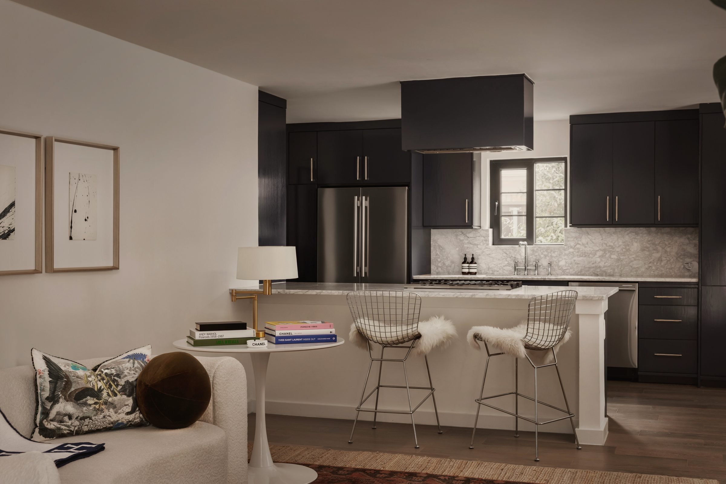 Kitchen with black cabinets and a black hood, white wire counter stools at a white island and a white sofa in front
