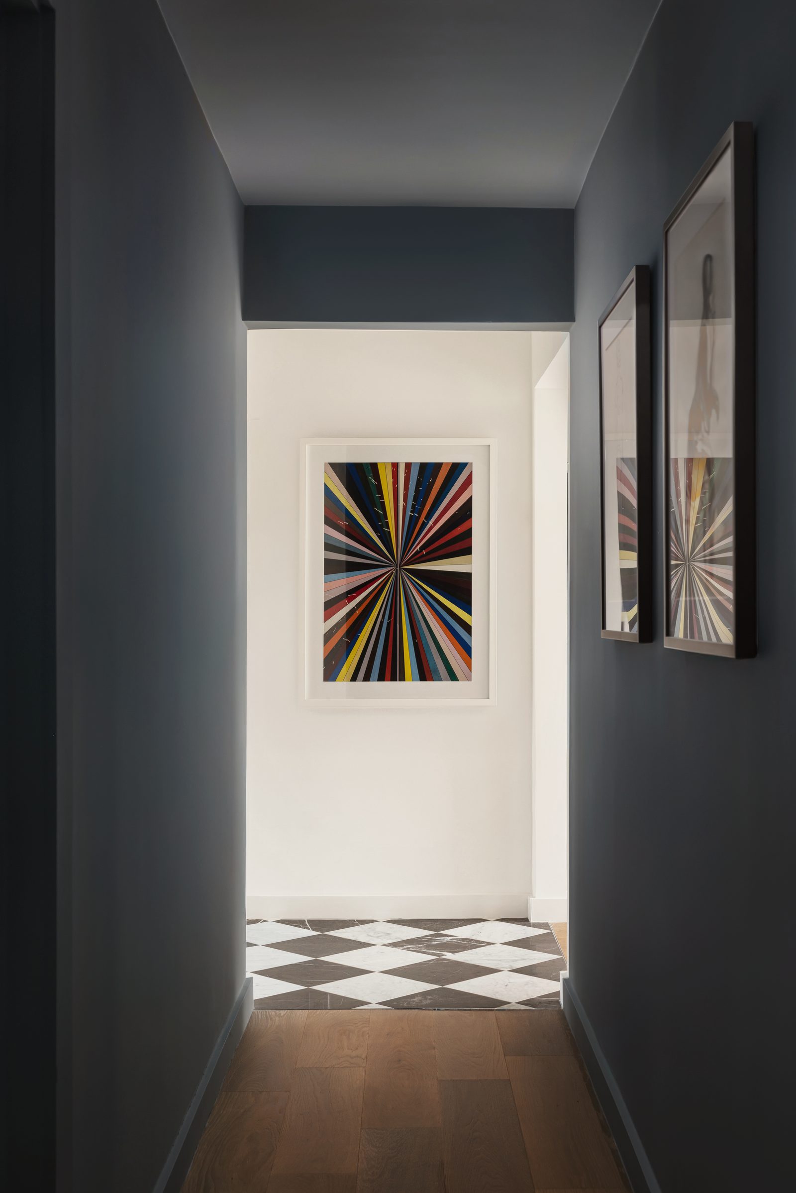 Charcoal hallway with framed black-and-white prints, a checkered floor and a colorful starburst print at the end